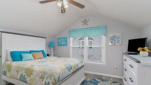 Un dormitorio con cama, ventilador de techo, ventana con contraventanas, cómoda y televisor.