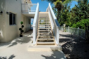 A staircase leading to a balcony with a white railing, surrounded by greenery and a clear sky.