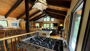 Une pièce au plancher de bois, équipée d’un baby-foot, d’un coin cuisine et de grandes fenêtres.