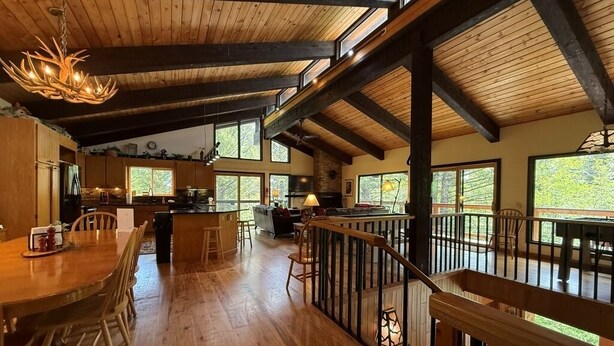 Une cuisine spacieuse avec des poutres en bois, un coin repas doté d’une grande table et un balcon agrémenté d’une balustrade.