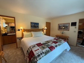 Ein Schlafzimmer mit einem Bett, zwei Nachttischen, einem Holzkopfende, einem Schminktisch, einem Spiegel und einem Bild an der Wand.