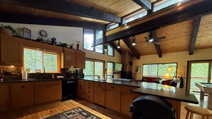 Une cuisine spacieuse dotée de meubles en bois, d’un grand îlot central et offrant une vue sur l’extérieur grâce à de nombreuses fenêtres.