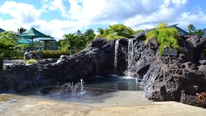 A waterfall feature with a pool, surrounded by tropical vegetation and a clear sky.