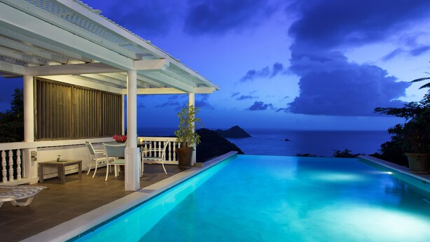 Un espace aménagé au bord de la piscine, avec vue sur l’océan, un coin salon abrité et une table avec des chaises.