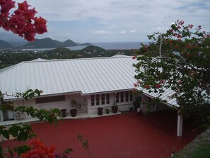 A building with a white roof and a red ground floor, surrounded by potted plants and flowers.