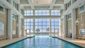 An indoor swimming pool with clear views through large windows, surrounded by lounge chairs.