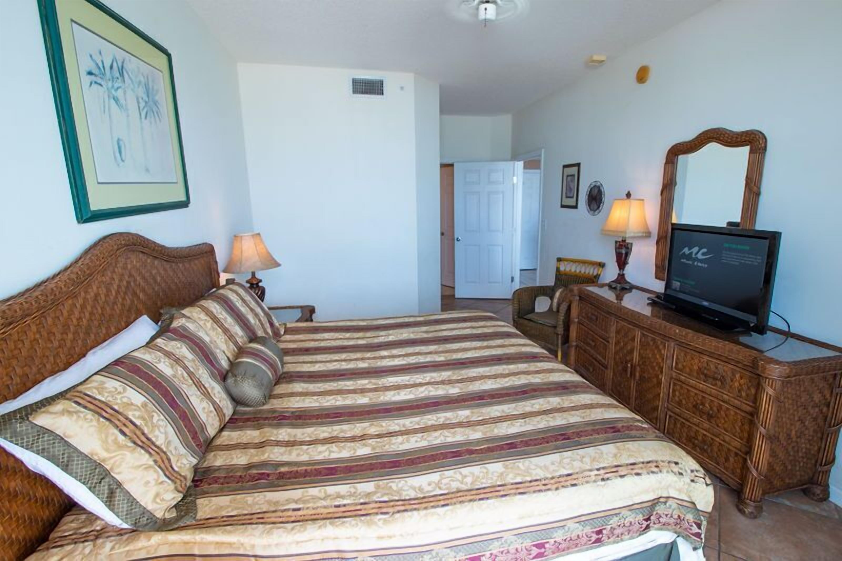 A hotel room with a large bed, a wooden dresser, a television, and a framed picture on the wall.