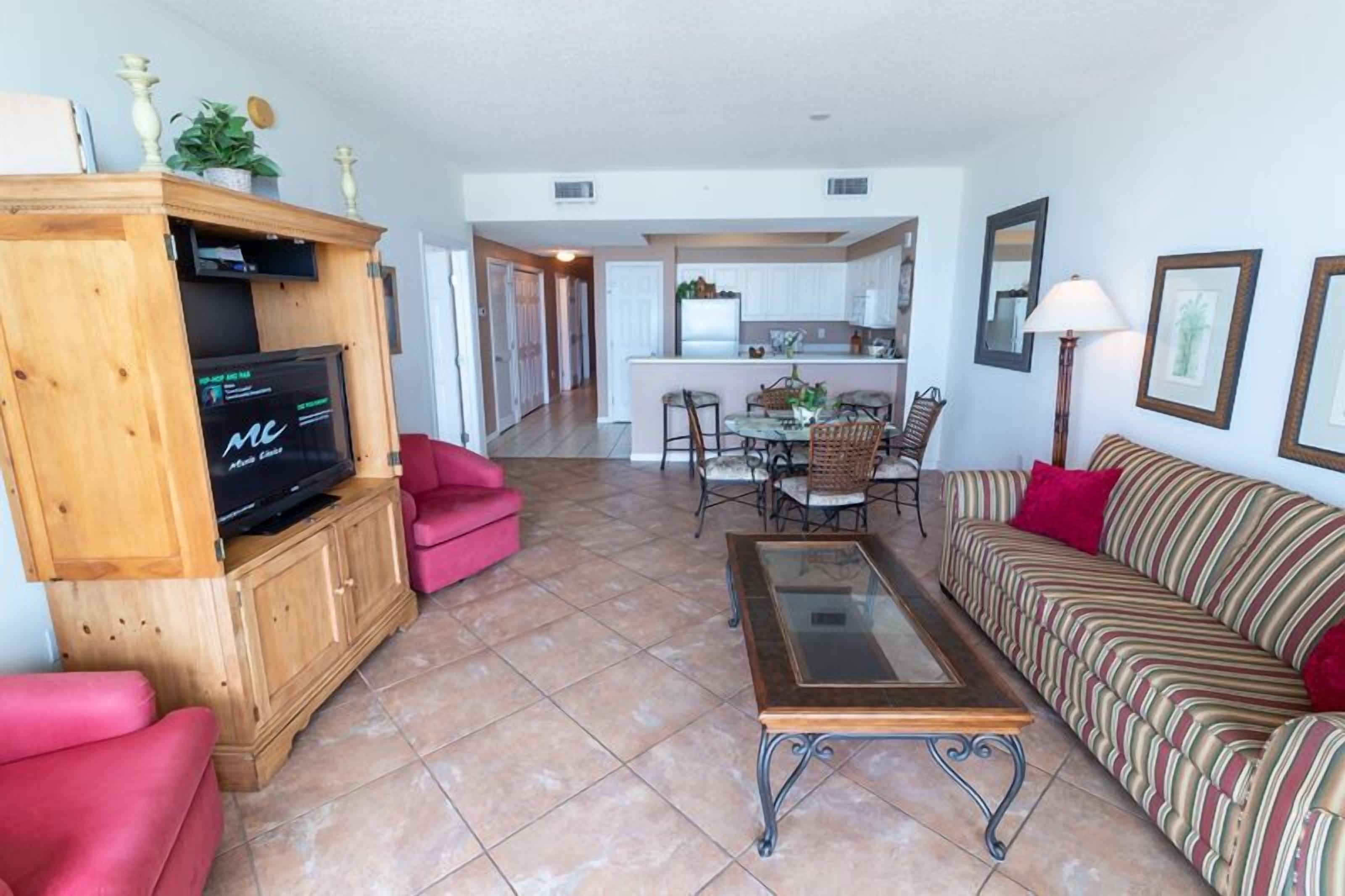 A living room with a TV, red sofa, striped couch, and a glass coffee table.