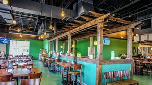 A restaurant with wooden tables and chairs, a counter with a green wall, and hanging pendant lights.