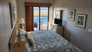 Une chambre d’hôtel avec un lit, une télévision, un balcon donnant sur la piscine et des tableaux encadrés au mur.