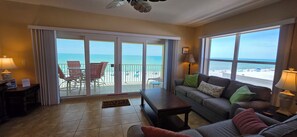 A living room with a sofa, a coffee table, a TV, and a balcony with a view of the beach. - Beachfront Bliss: A Guest Favorite for Flip-Flops, Beach Days & Stunning Sunsets (Indian Rocks Beach)