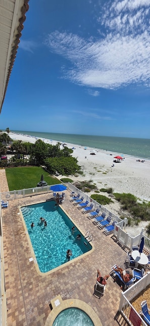 A pool area with a view of the beach, lounge chairs, and a clear sky. - Beachfront Bliss: A Guest Favorite for Flip-Flops, Beach Days & Stunning Sunsets (Indian Rocks Beach)