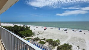 Vista a la playa desde un balcón con barandilla, sombrillas y sillas de descanso.