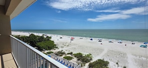 A beach view from a balcony with a railing, beach umbrellas, and lounge chairs. - Beachfront Bliss: A Guest Favorite for Flip-Flops, Beach Days & Stunning Sunsets (Indian Rocks Beach)