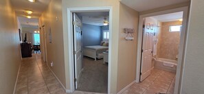A hallway leading to a bedroom with a bed, a bathroom with a bathtub, and a dining area with a table and chairs. - Beachfront Bliss: A Guest Favorite for Flip-Flops, Beach Days & Stunning Sunsets (Indian Rocks Beach)