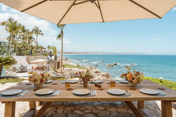 A wooden table set for dining with a view of the ocean and palm trees.