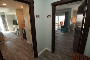 A hallway with wooden flooring, a television in the background, and two doors labeled 6534 and 6532. - True 1 BR with full kitchen, Luau 6532 by Skis and Seas | South Gulf facing (Destin)
