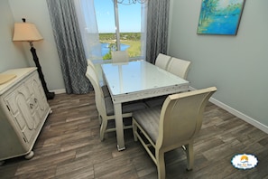 A dining area with a table and chairs, a lamp, and a view of a landscape through a window. - True 1 BR with full kitchen, Luau 6532 by Skis and Seas | South Gulf facing (Destin)