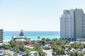 A coastal hotel with a view of the ocean, a parking lot, and a tall building in the background. - True 1 BR with full kitchen, Luau 6532 by Skis and Seas | South Gulf facing (Destin)