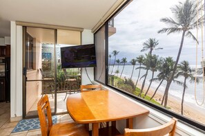 A dining area with a large window overlooking a beach with palm trees.