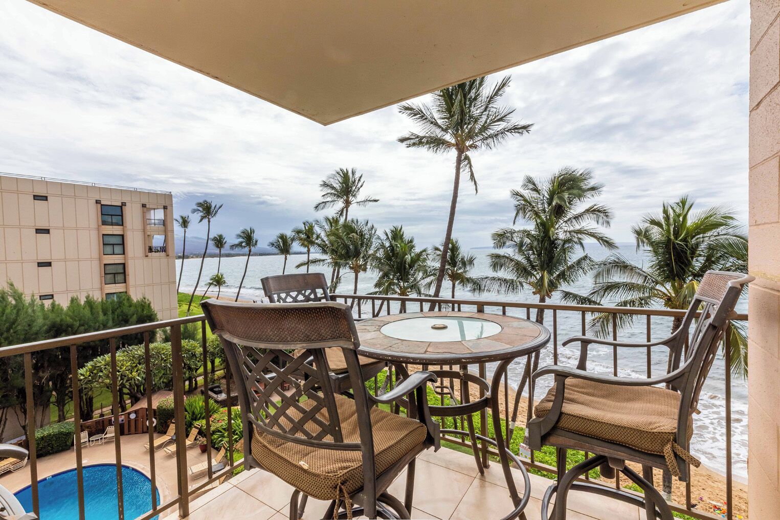 A balcony with a view of the ocean, equipped with wicker chairs and a glass-top table.