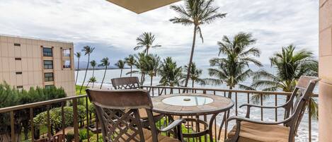 A balcony with a view of the ocean, equipped with wicker chairs and a glass-top table.