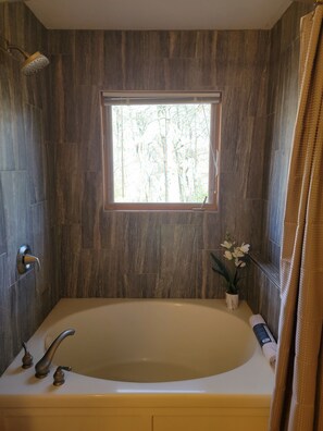 A bathroom with a large bathtub, a window with a view of trees, a showerhead, and a towel rack.