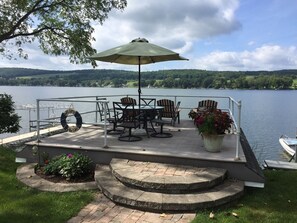 Relax on the lakeside deck with a table and chairs under a spacious umbrella, surrounded by a garden and a serene lake view.