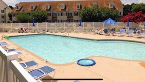 A swimming pool with lounge chairs and umbrellas, surrounded by a fence and buildings in the background.