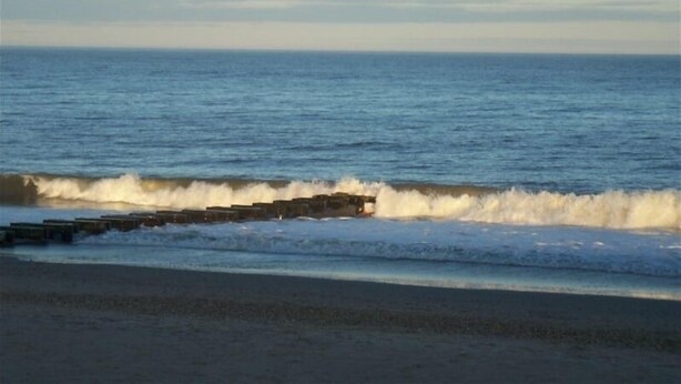 A beach with waves crashing onto a wooden breakwater.