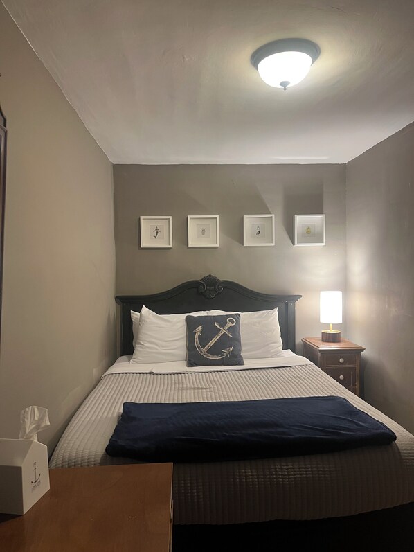 Un dormitorio ordenado con cama, mesita de noche, lámpara y cuadros en la pared.
