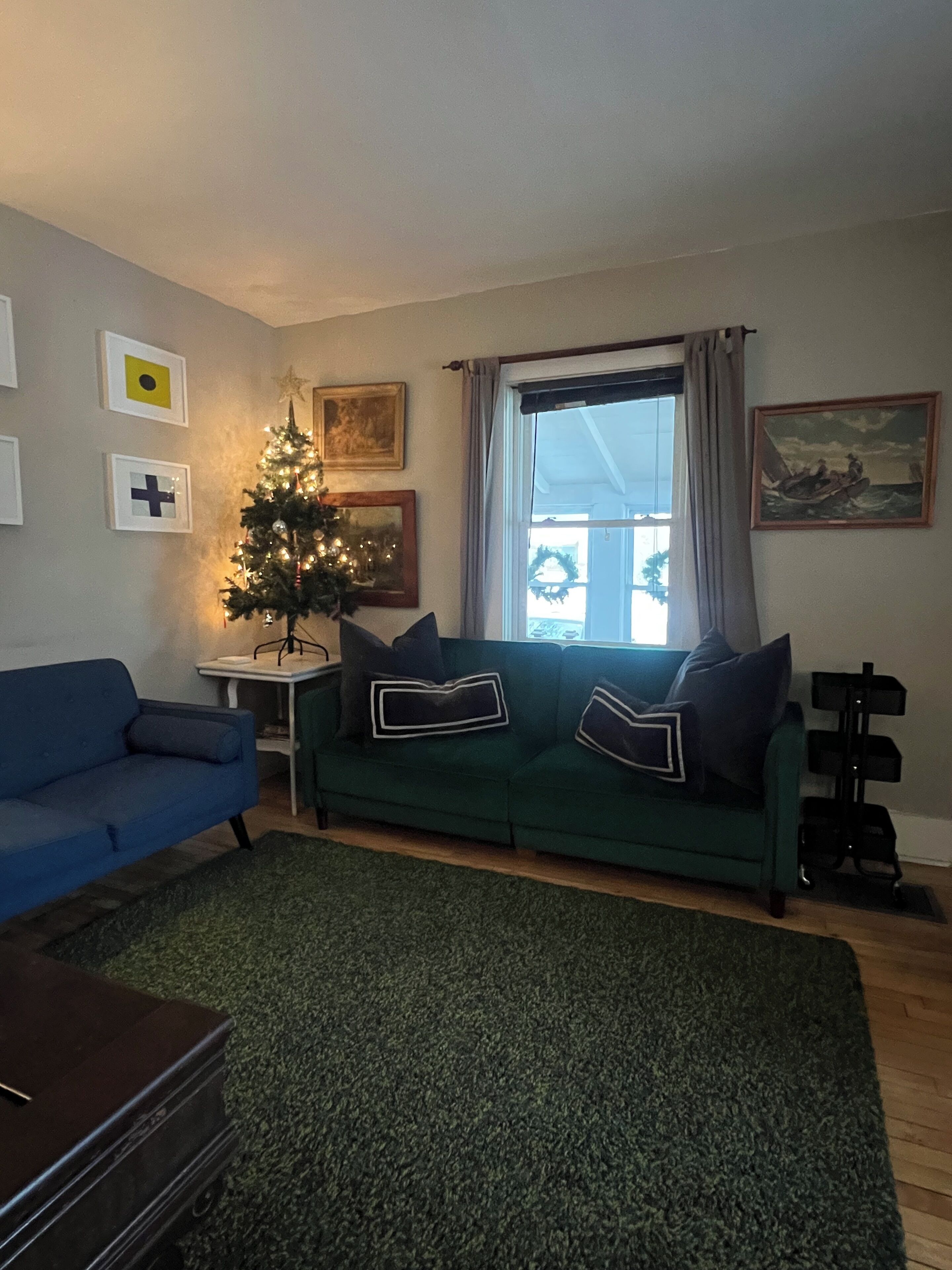 En stue med en grøn sofa, en blå sofa, et juletræ og et vindue med gardiner.