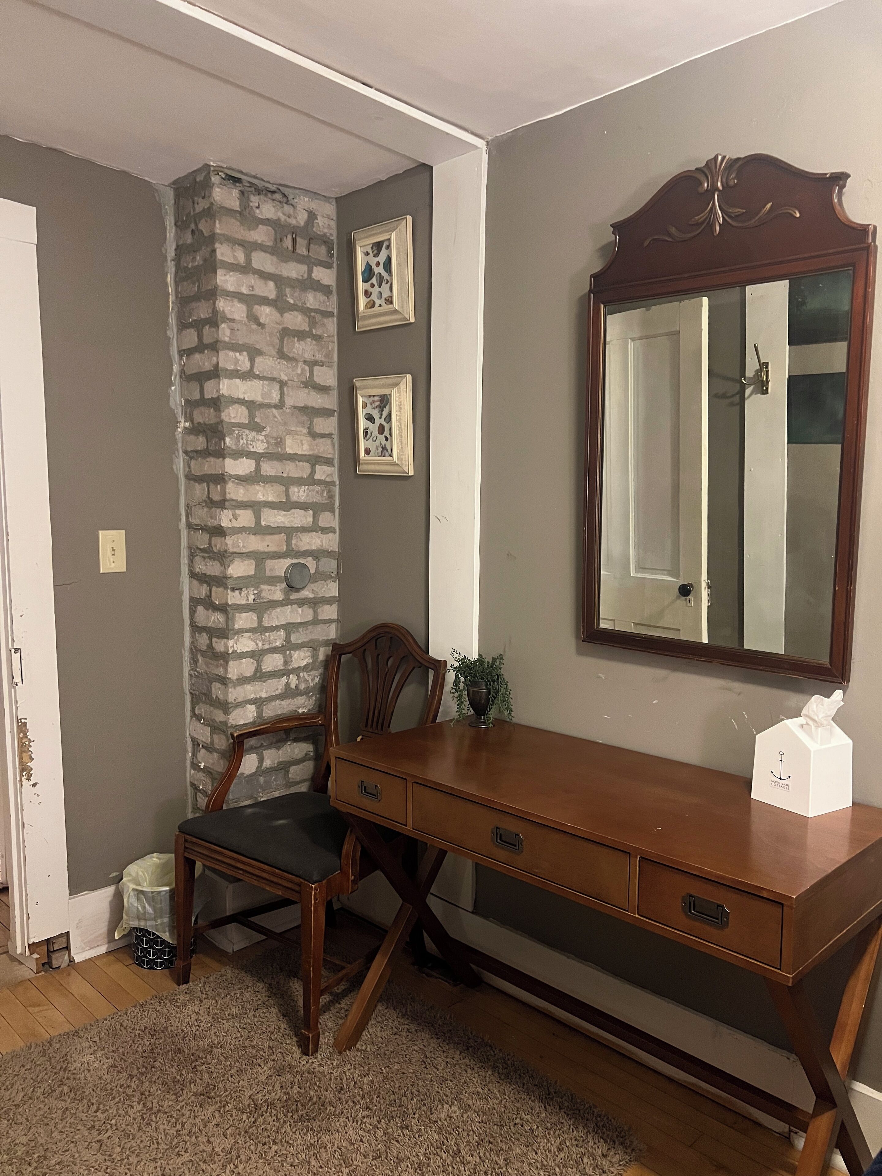 A room with a wooden desk, a chair, a large mirror, and a stone wall.
