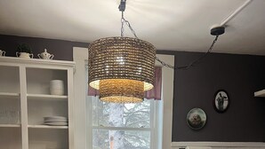 Un coin repas avec une table ronde et quatre chaises, un luminaire suspendu, une fenêtre donnant sur des arbres et un buffet blanc contenant de la vaisselle.