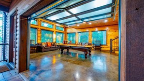 Un espace intérieur spacieux comprenant une table de billard, des sièges confortables et de grandes fenêtres laissant entrer la lumière naturelle.