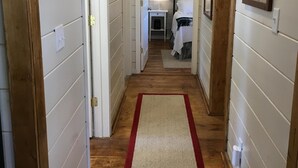 Ein schmaler Korridor mit Holzböden und weißen Wänden, der zu einem Schlafzimmer mit Bett und Nachttisch führt.