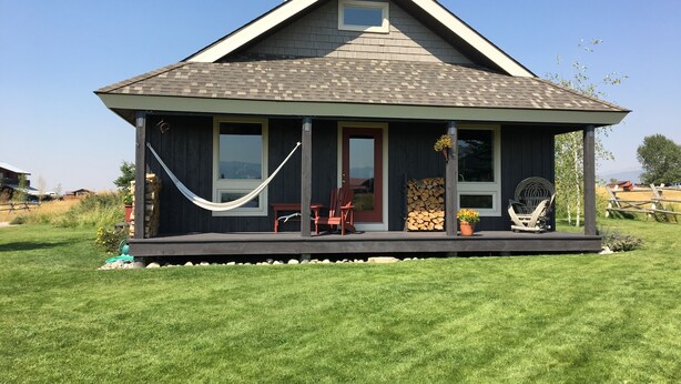Une maison avec un toit en pente, une véranda avec un hamac et une pile de bois de chauffage.