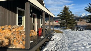 Une cabane dotée d’une terrasse en bois et d’une cheminée en pierre, entourée de neige et de montagnes.