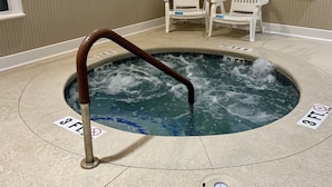 Un jacuzzi con una escalera de madera, dos sillas blancas y un letrero de precaución en la pared.