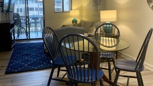 Una sala de estar con una mesa de comedor de vidrio, sillas negras, un tapete azul y un sofá.