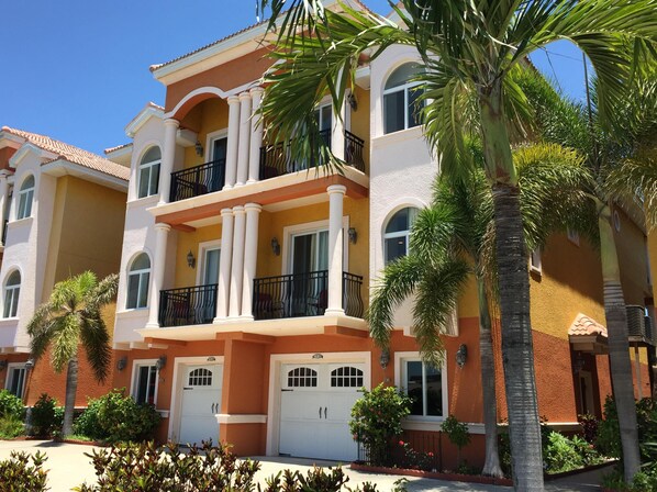 A multi-story residential building with balconies, large windows, and a well-maintained garden with palm trees and shrubs.