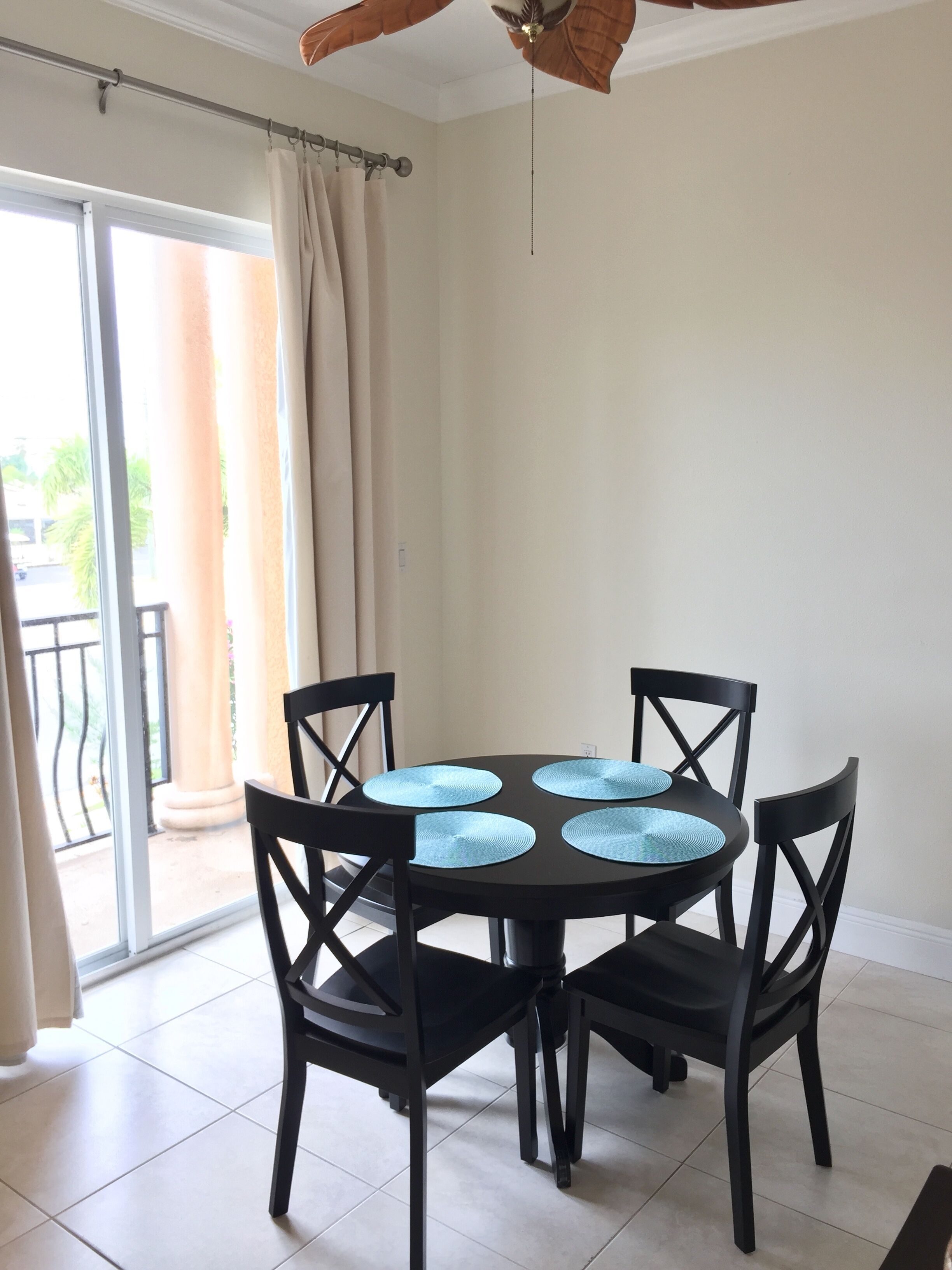 A dining area with a round table, four chairs, and a ceiling fan.