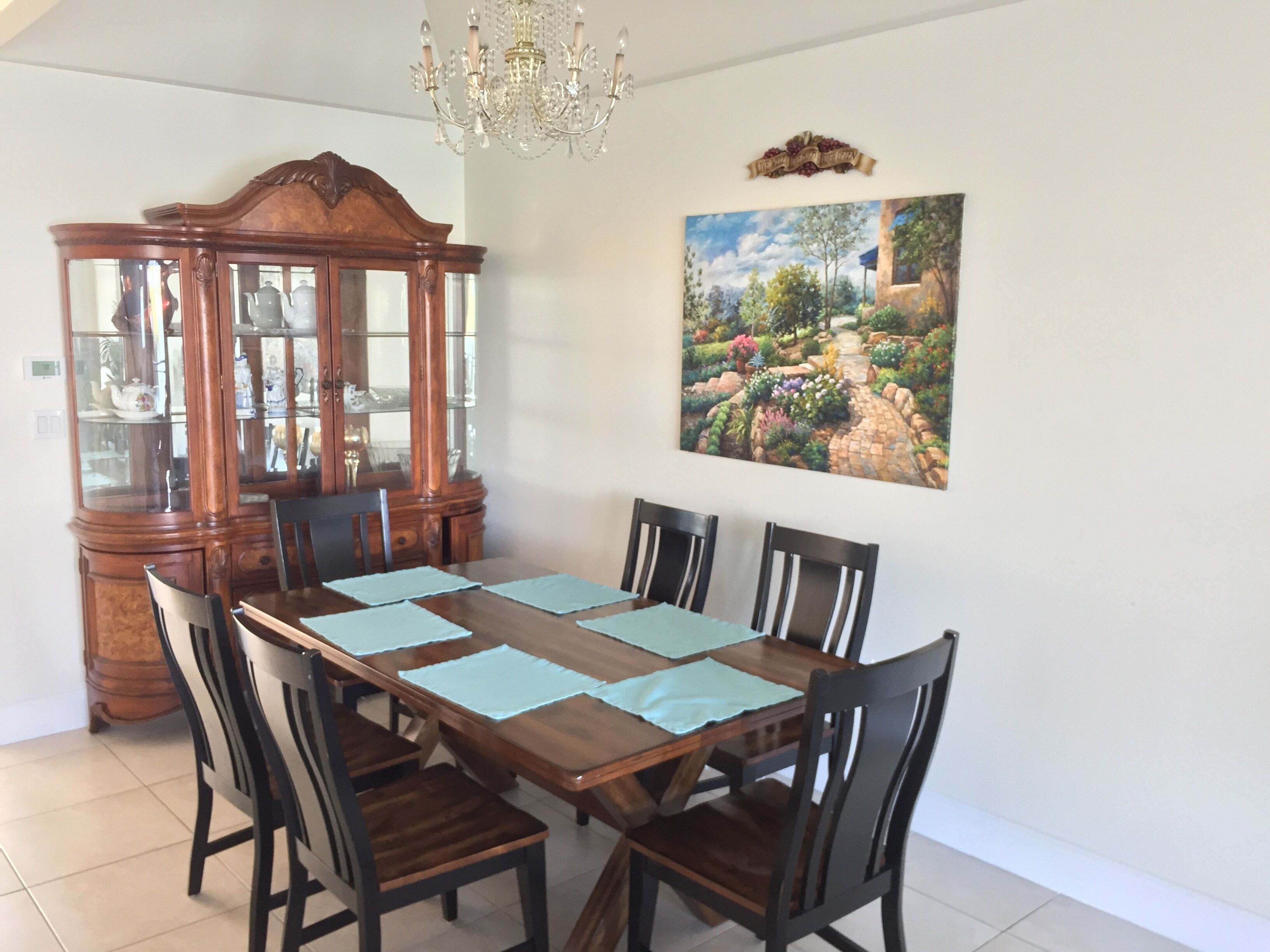A dining room with a wooden table, six chairs, a china cabinet, and a painting of a garden on the wall.