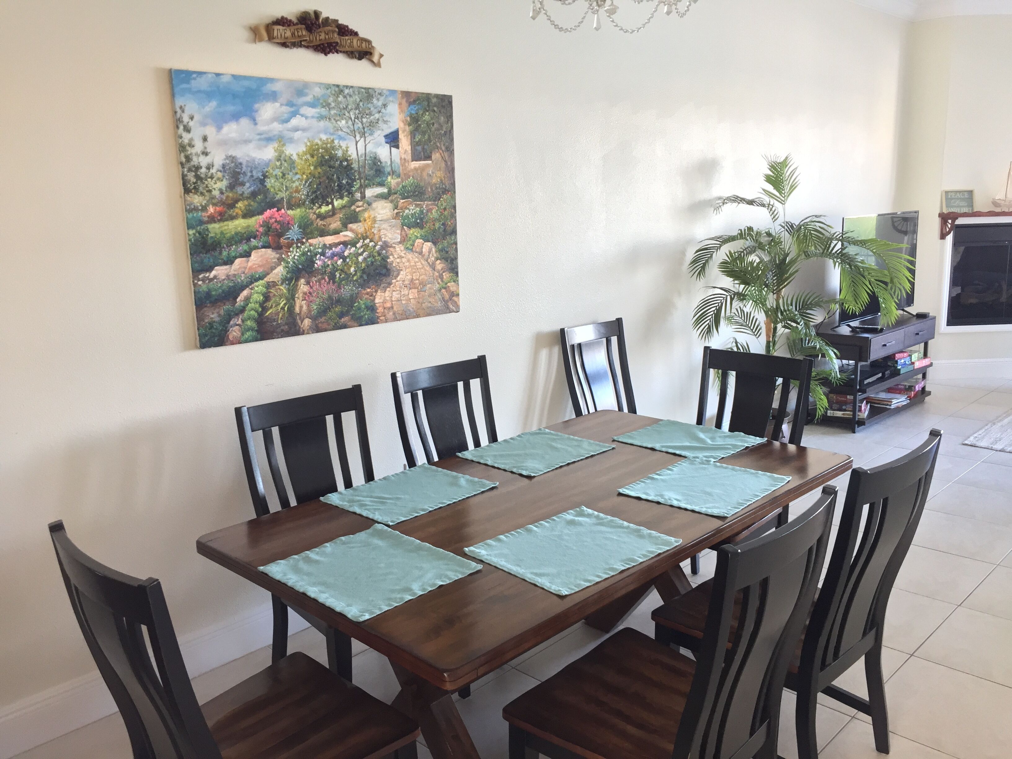 A dining area with a wooden table, six chairs, and green placemats.