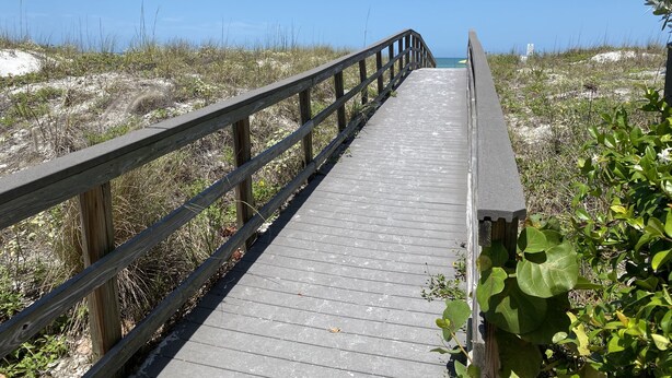 A wooden boardwalk leading to a beach with sandy dunes and sparse vegetation.