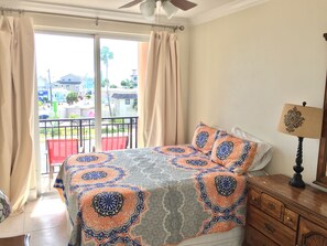 A bedroom with a bed, a nightstand, a lamp, and a view of the outside.