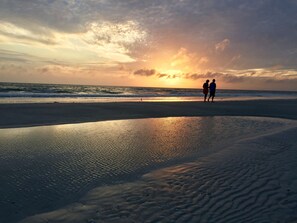 A beach scene with two people walking along the shore during sunset.