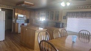 A kitchen with wooden cabinets, a microwave, a stove, a dining table with chairs, and a ceiling fan. - Mountain vacation getaway/Hunters paradise (Young)
