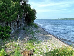 Un paisaje natural con costa rocosa, abundante vegetación y una masa de agua tranquila.