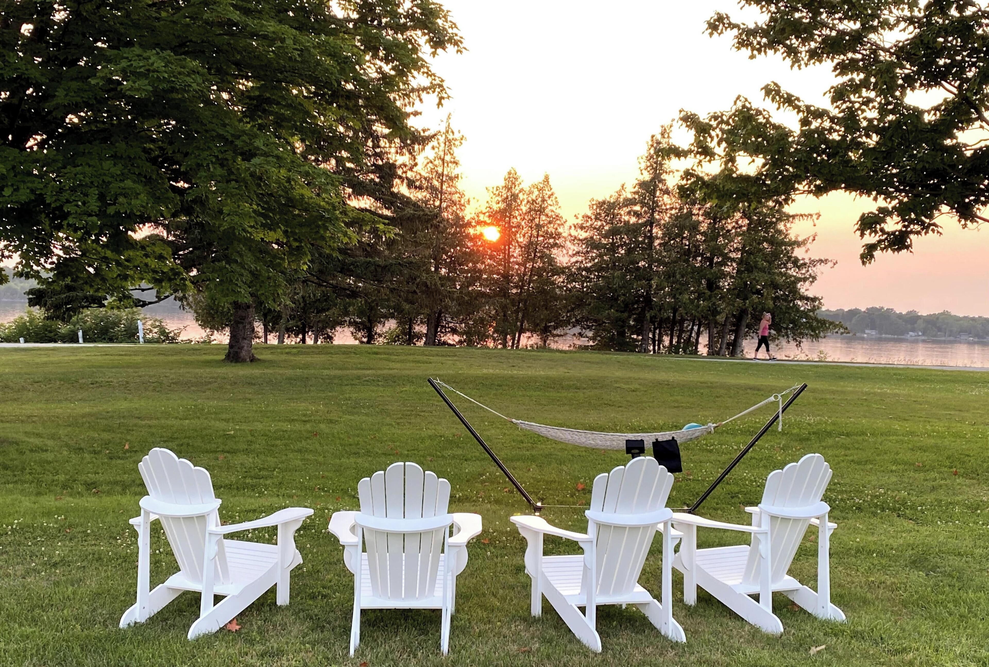 Uma área gramada com quatro cadeiras Adirondack brancas e uma rede.